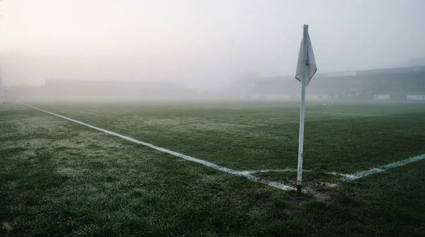 Der Rand eines Spielfelds mit weißer Linie und Eckfahne bei Nebel am frühen Morgen, ohne Menschen.