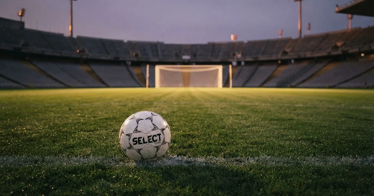 Ein Fußball liegt im Strafraum direkt vor dem Tor mit Netz, im Hintergrund leere Ränge bei Dämmerung.
