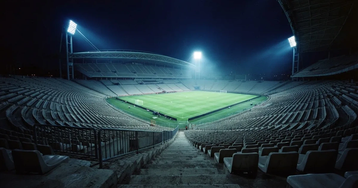 Leere Sitzreihen eines großen Stadions unter Flutlicht, dahinter die ferne Sicht auf den hell beleuchteten Rasen nach Sonnenuntergang.