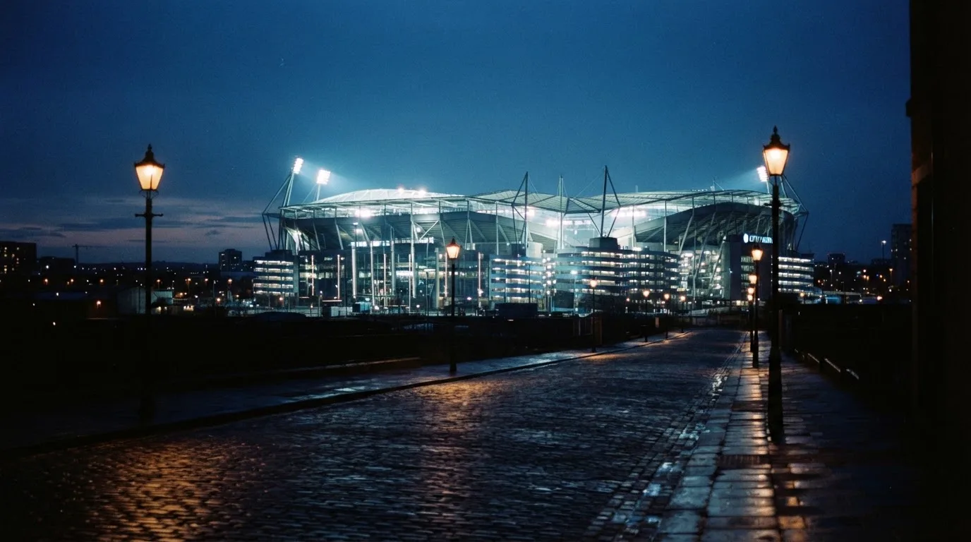 Ein Stadion unter Flutlicht aus der Ferne gesehen, davor eine dunkle Straße mit Laternen und ohne Menschen.