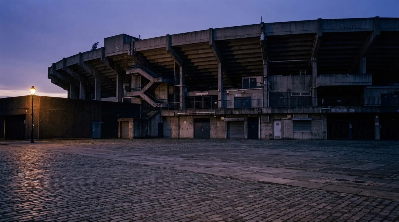 Die Rückseite einer Tribüne bei Dämmerung, davor ein menschenleerer Vorplatz mit Pflastersteinen.