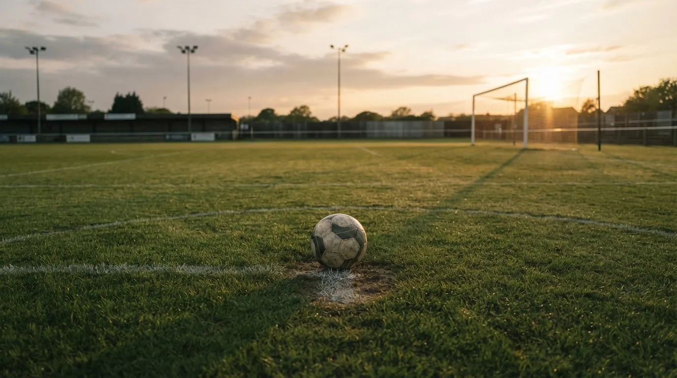 Ein Fußball liegt auf dem Elfmeterpunkt eines leeren Platzes im Abendlicht.