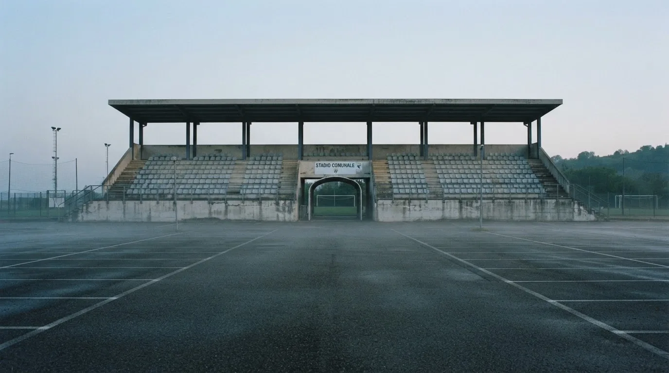 Eine leere Tribüne eines kleinen Stadions am frühen Morgen, aus der Ferne über einen menschenleeren Parkplatz fotografiert.