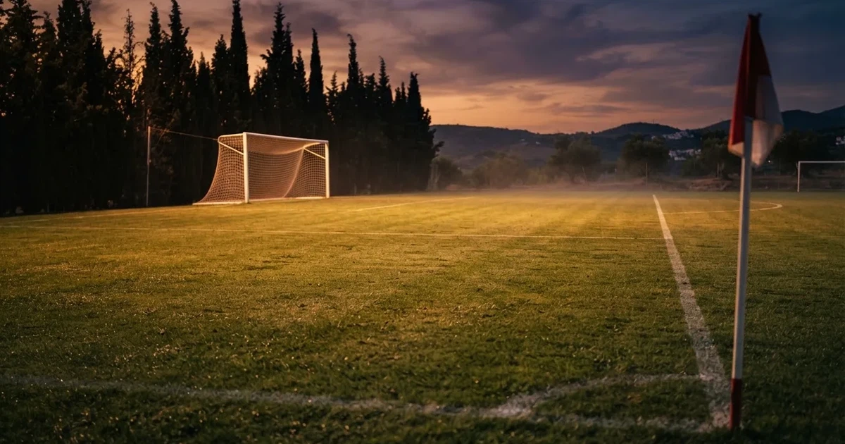 Ein Fußballtor mit Netz auf einem leeren Platz im Abendlicht, der Rasen frisch gemäht, im Hintergrund Zypressen.