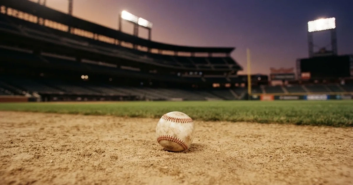 Ein Baseball liegt auf dem hellen Sand des Infields, im Hintergrund eine große Tribüne in der Abenddämmerung.