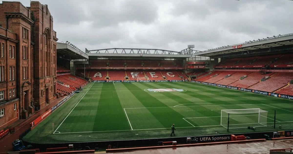 Ein englisches Fußballstadion mit rotbraunen Backsteintribünen unter bedecktem Himmel, davor ein nasser Rasen mit Spielfeldlinien.