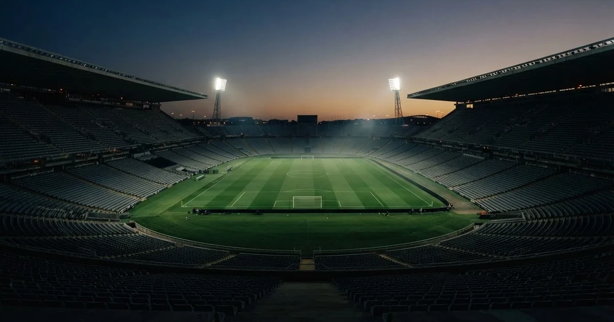 Ein Fußballstadion am Abend unter Flutlicht aus der Ferne gesehen, die Tribünen sind leicht beleuchtet und der Himmel dunkelblau.